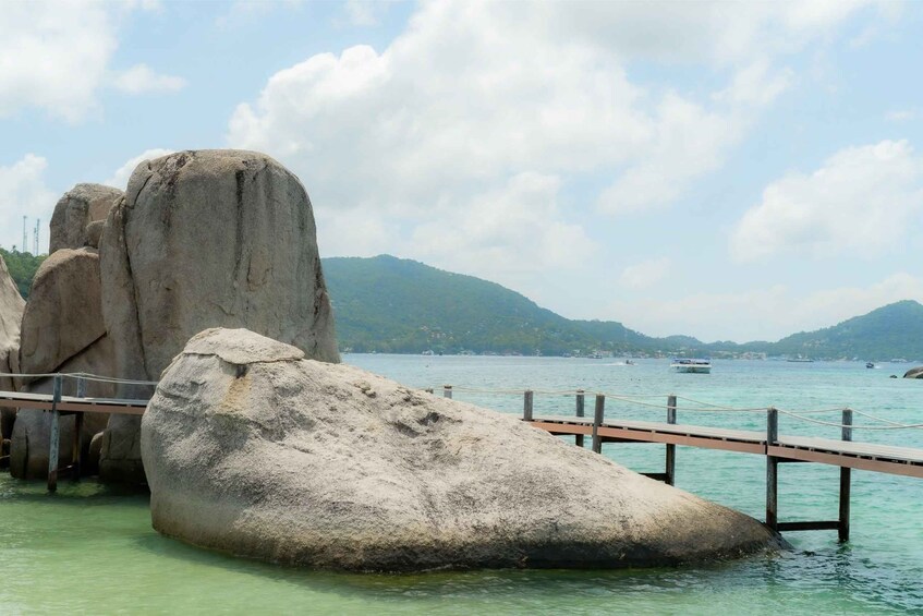 A rocky coastline with a wooden pier extending into turquoise waters, surrounded by mountains and clear skies. 5