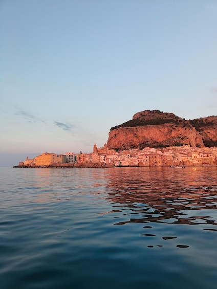 A coastal town with buildings along the waterfront, a prominent cliff, and calm water reflecting the structures. 2