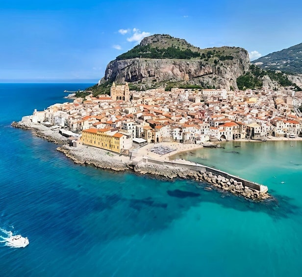 A coastal town with a prominent hill, a sea wall, and a clear blue sky. 3