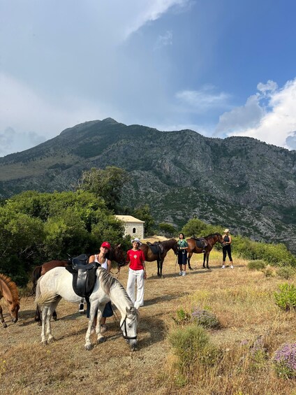 A group of people with horses in a mountainous area with a stone building in the background. 3