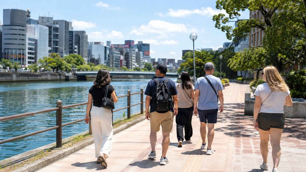 A group of people walking along a riverside path with a cityscape in the background. 3