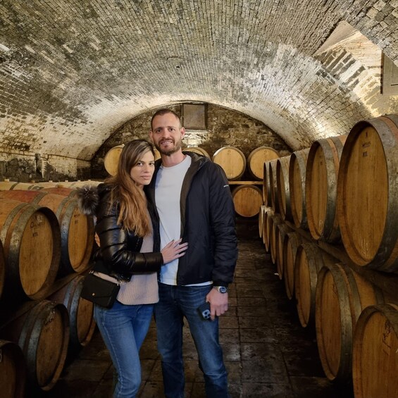 A man and woman standing in a wine cellar with wooden barrels. 5