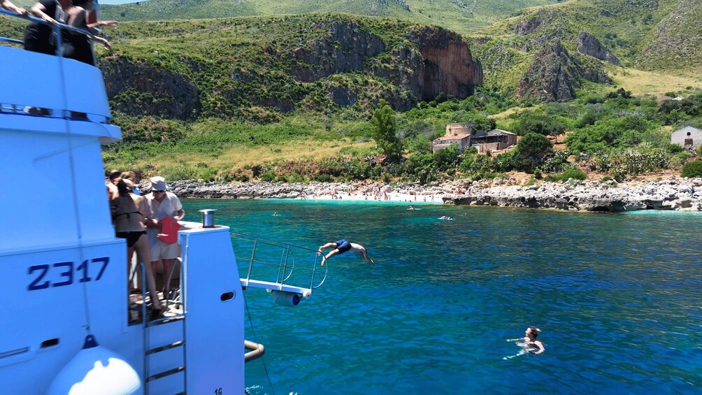 A clear blue sea with people swimming and a rocky coastline. 2