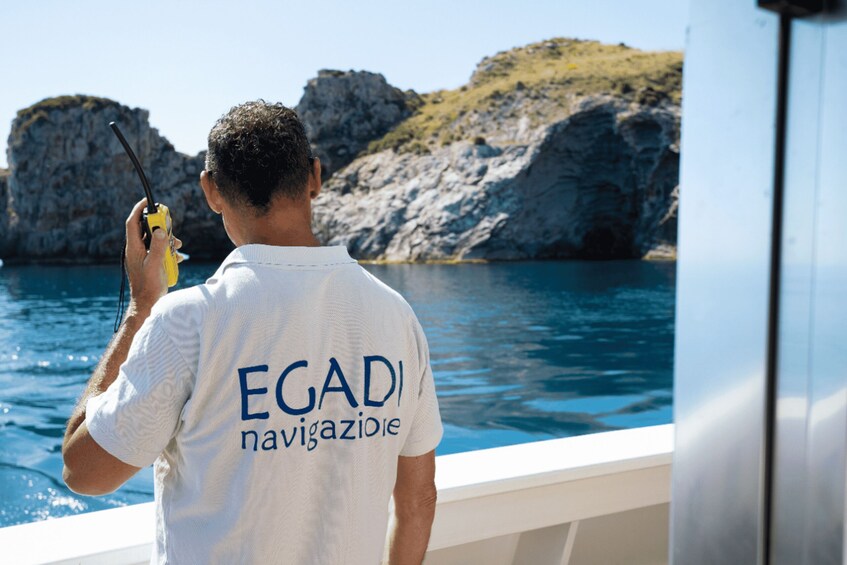 A person on a boat holding a walkie-talkie, with rocky cliffs and water in the background. 3