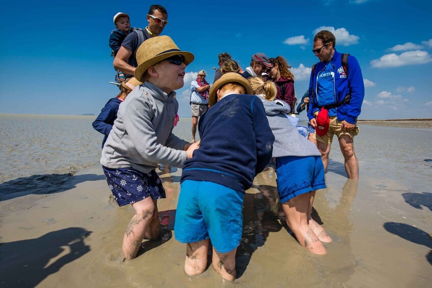A group of people, including children, engaging in an activity on a sandy beach with shallow water. 4