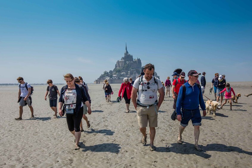 A group of people walking on a sandy beach with a historic castle in the background. 2