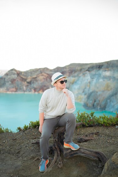 A person sitting on a tree stump by a coastal cliff with a turquoise sea in the background. 4