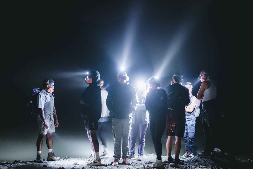 A group of people standing on a rocky surface with bright lights in the background. 3