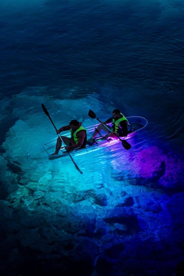 Two people kayaking on a frozen body of water with colorful lights. 1