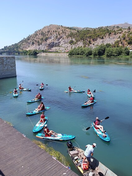 People kayaking on a calm river, surrounded by a hilly landscape. 4