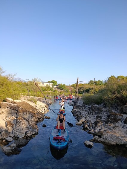 A group of people paddling kayaks on a narrow river surrounded by rocky banks and greenery. 3