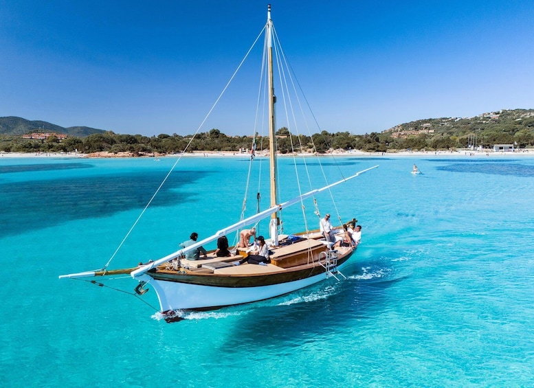 A sailboat on turquoise waters with a beach and hills in the background. 5