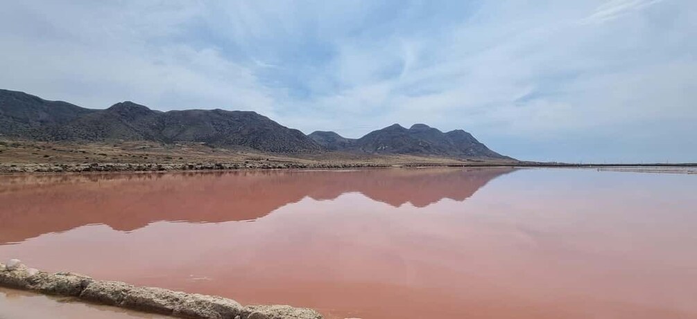 A calm lake with a reddish hue, surrounded by mountains under a clear sky. 1