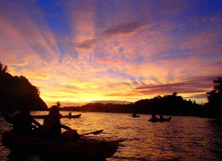 A sunset over a body of water with kayaks and people. 1