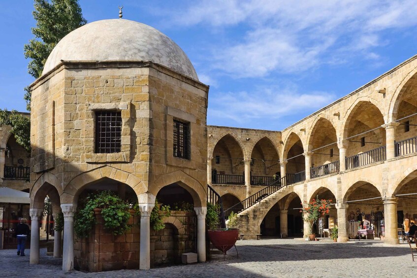 A historic courtyard with a dome and arches, featuring stone buildings and a cobblestone ground. 5