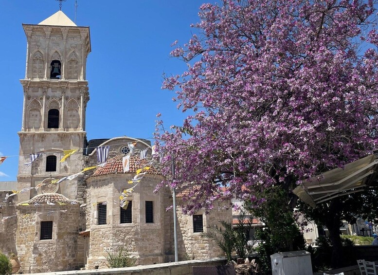 A historic stone building with a bell tower, surrounded by blooming pink flowers. 1