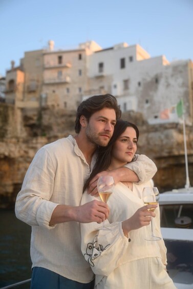 A couple on a boat with a rocky coastline and buildings in the background. 4