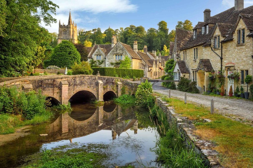 A stone bridge over a calm river, surrounded by lush greenery and traditional stone buildings with steep roofs. 2