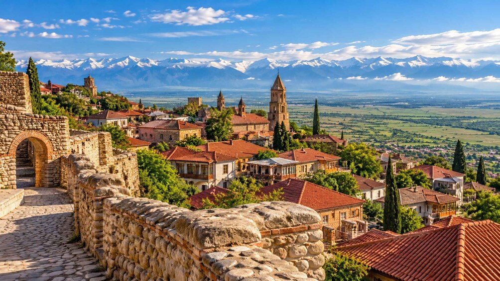 A historic town with stone walls, red-roofed buildings, and a prominent church tower. 1