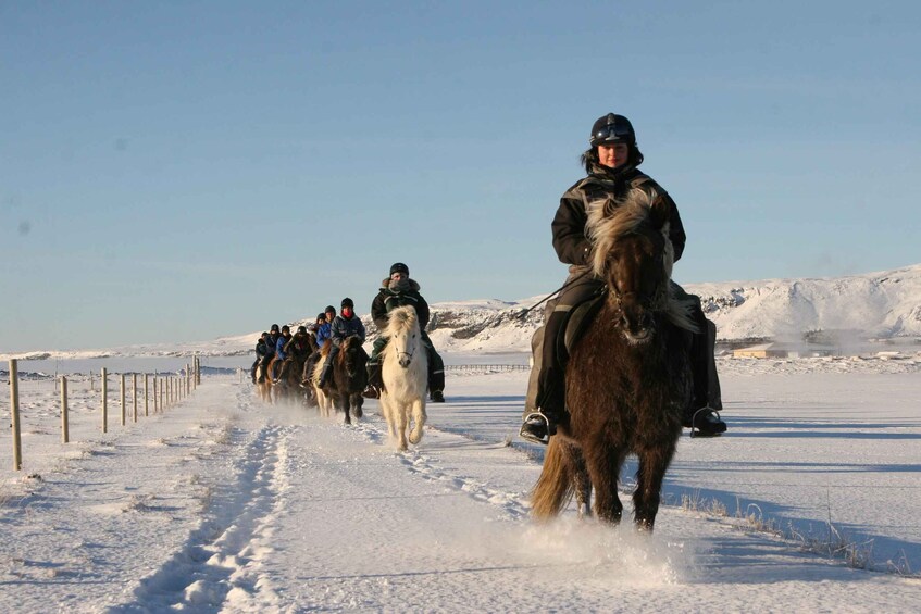 A group of people horseback riding on a snow-covered path. 4