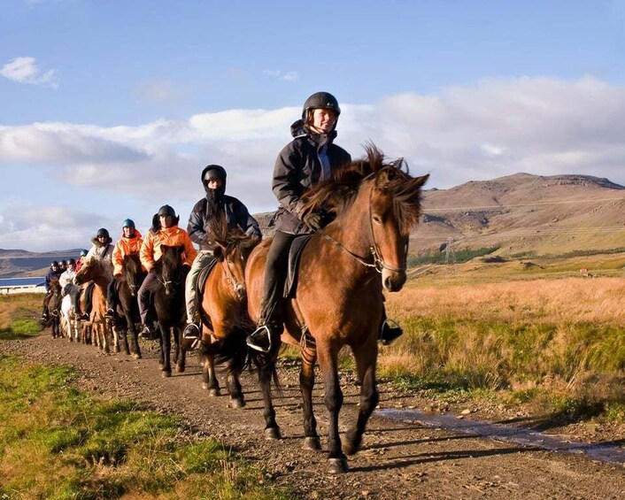 A group of riders on horses along a dirt path in a hilly landscape. 1