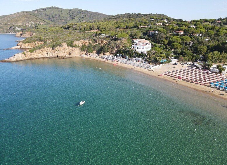 A coastal area with clear blue water, a sandy beach, and a hilly landscape with buildings. 2