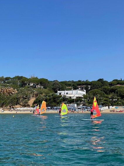 A beach with people windsurfing, a clear blue sky, and buildings in the background. 1