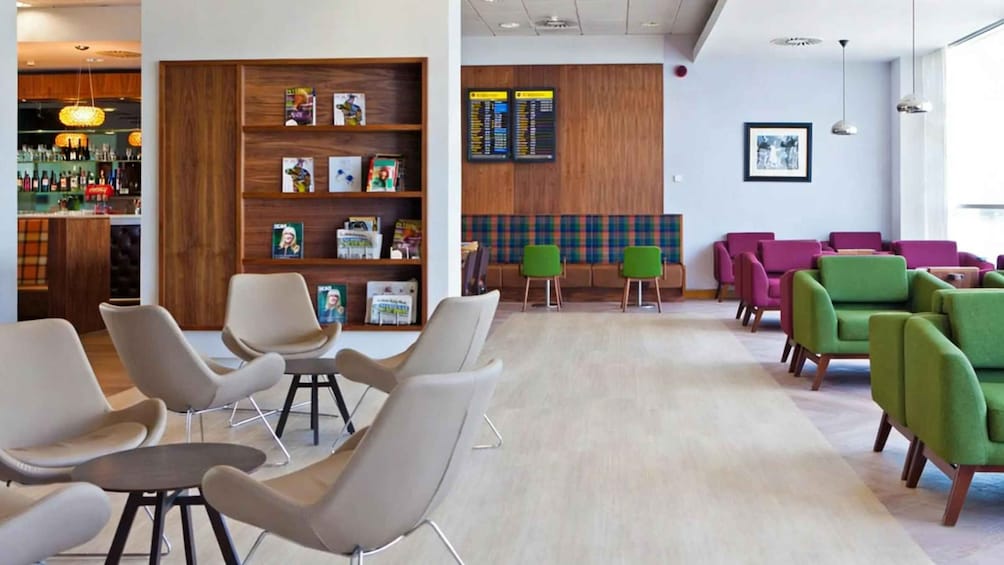 A modern waiting area with green and beige chairs, wooden shelves with magazines, and a bar area with bottles. 4