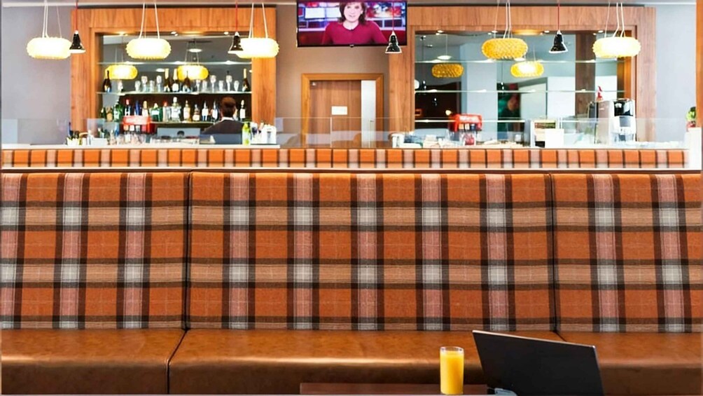 A bar area with a plaid booth seating, a television screen, and hanging pendant lights. 3