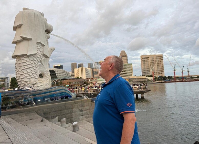 A man in a blue shirt standing by a water feature with a dragon sculpture. 3