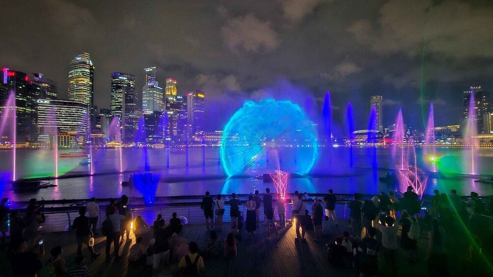 A nighttime cityscape with illuminated buildings and a water fountain show. 5
