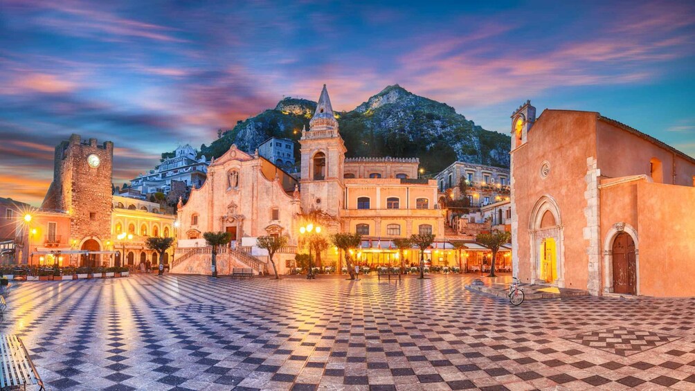 A historic town square with a checkered pavement, a prominent church with a bell tower, and a castle-like structure. 5