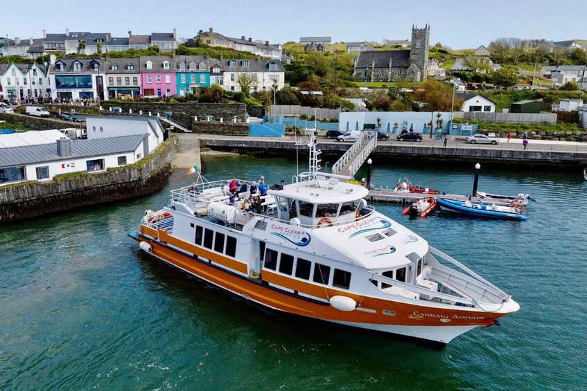 A ferry named 'Cape Clear Ferries' docked at a harbor with colorful buildings and a church in the background. 2