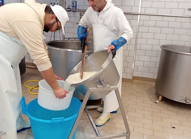 Two individuals in a kitchen setting, one pouring a liquid into a container and the other holding a large metal bowl. 2