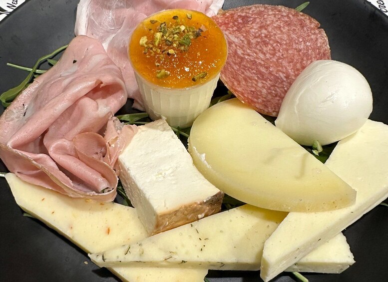 A charcuterie board with various cheeses, cured meats, and a small dish of chutney. 3