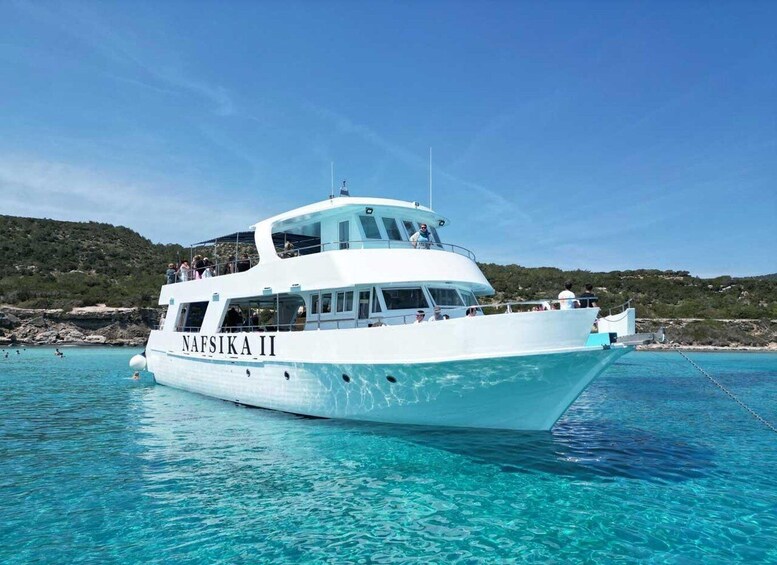 A white boat named 'NAFSIKA II' on clear blue water with a rocky coastline in the background. 5