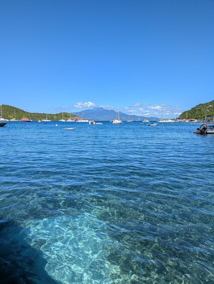 A clear blue sea with boats, a mountain, and a green hillside. 3
