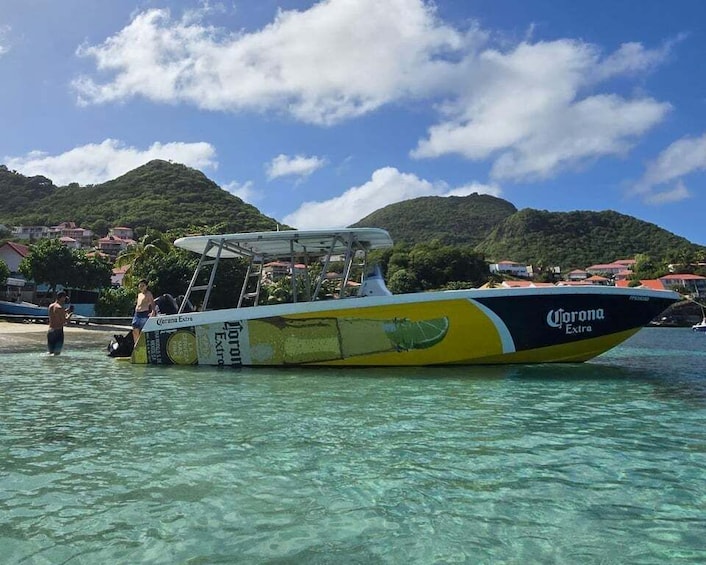 A yellow and black boat with 'Corona Extra' branding on a clear blue sea with a mountainous backdrop. 4
