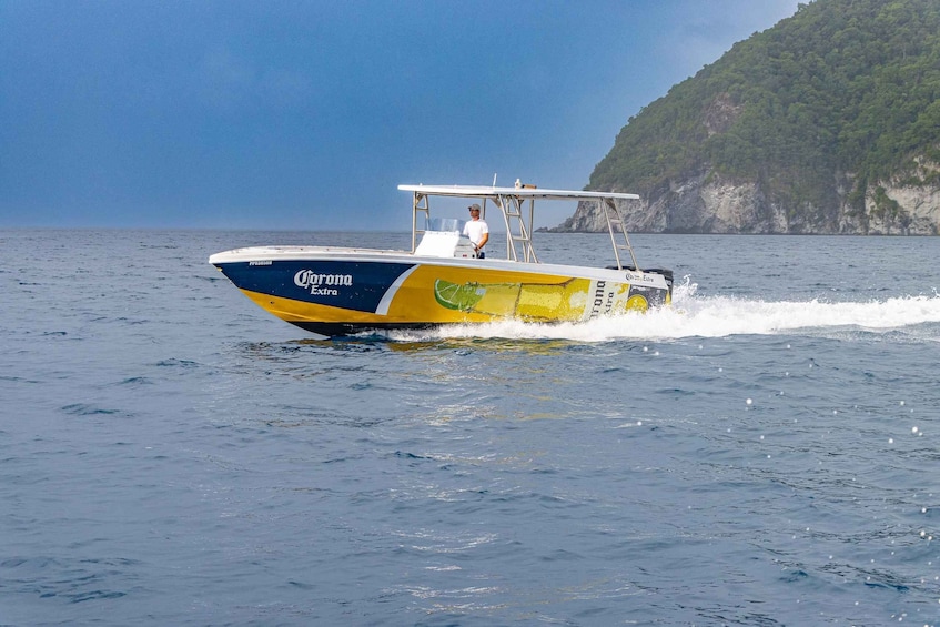 A speedboat with a blue and yellow hull, branded with Corona Extra, moving through calm waters with a clear sky and a rocky coastline in the background. 2