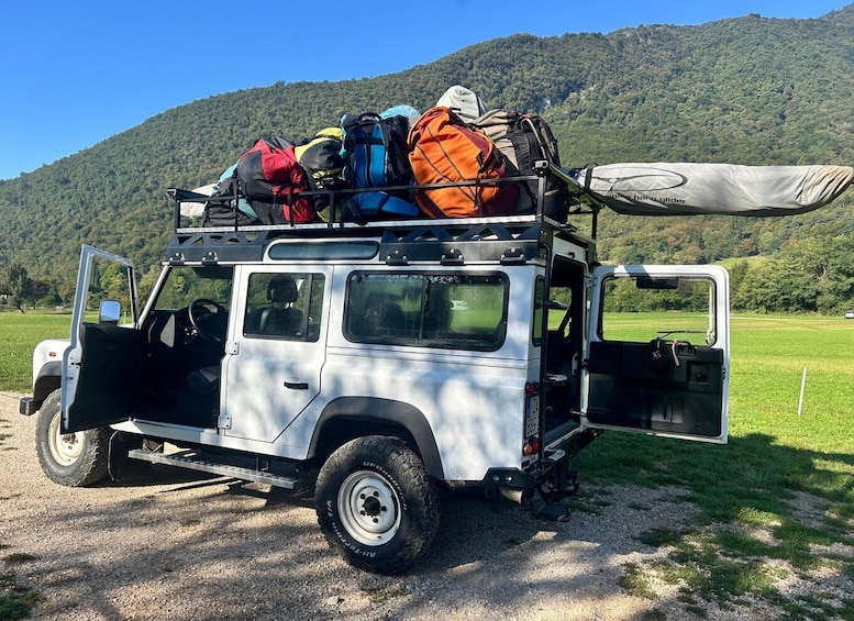A white off-road vehicle with a roof rack loaded with camping gear and a tent. 3