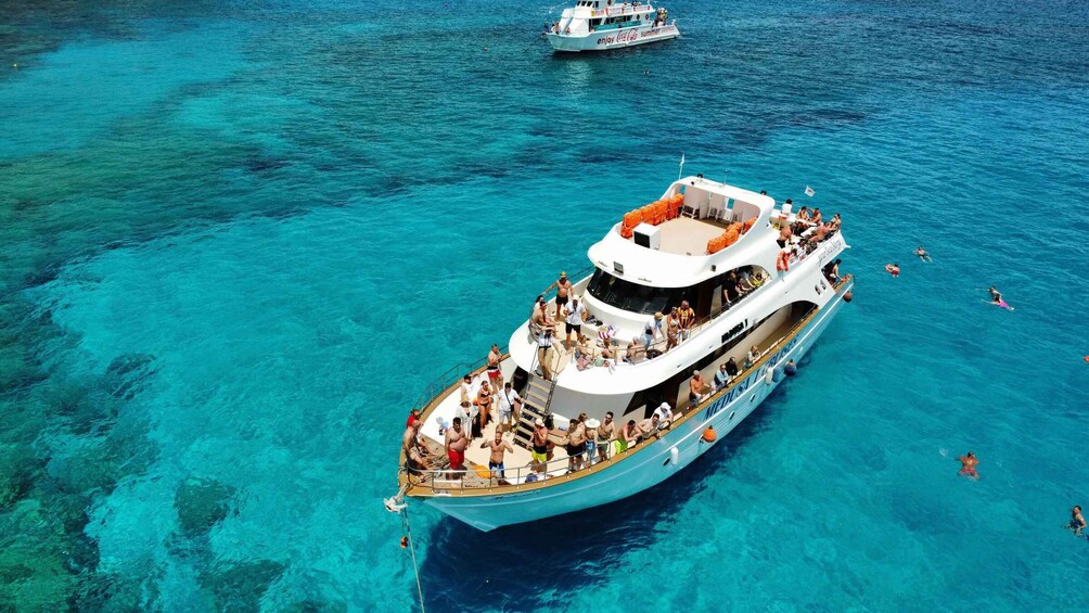 A large boat with people on deck and in the water, surrounded by clear blue sea. 4