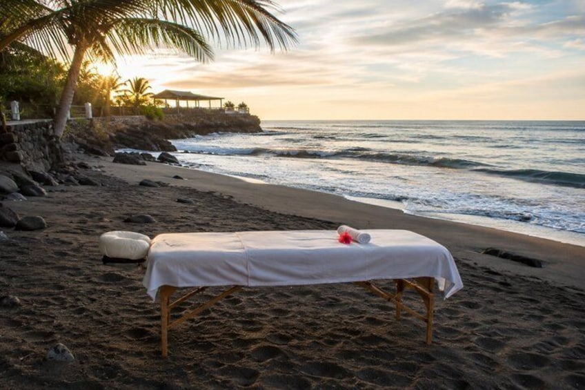 A beach with a massage table set up under a palm tree. 3