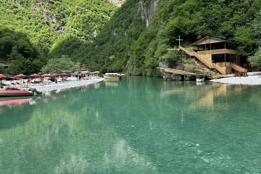 A serene lake with clear water, surrounded by lush greenery and a wooden structure with a staircase leading up to it. 4