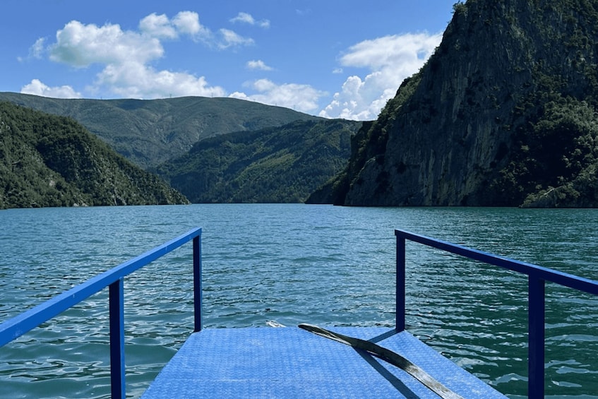 A lake with a blue railing in the foreground and steep, forested hills in the background. 3