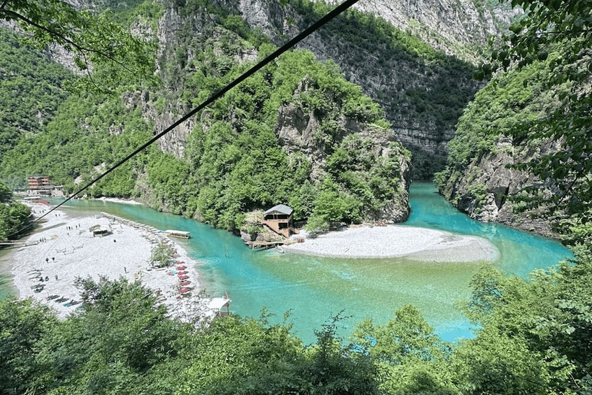 A river winding through a mountainous area with a small island and a beach with people. 1
