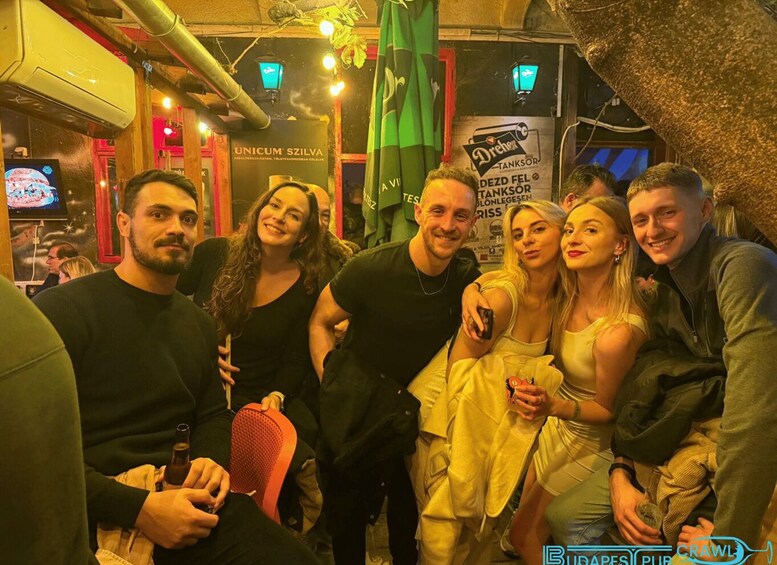 A group of people in a bar with a sign for 'UNICUM SZILVA' and 'Dreher TANKSOR'. 4
