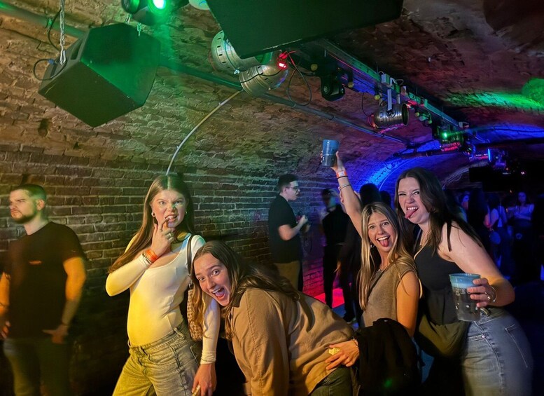 A group of people at a social event in a dimly lit venue with brick walls and hanging lights. 5