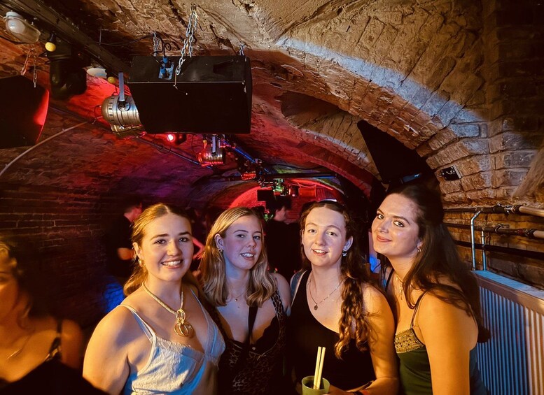 A group of people in a dimly lit, vaulted stone room with exposed brick walls and a ceiling-mounted projector. 2