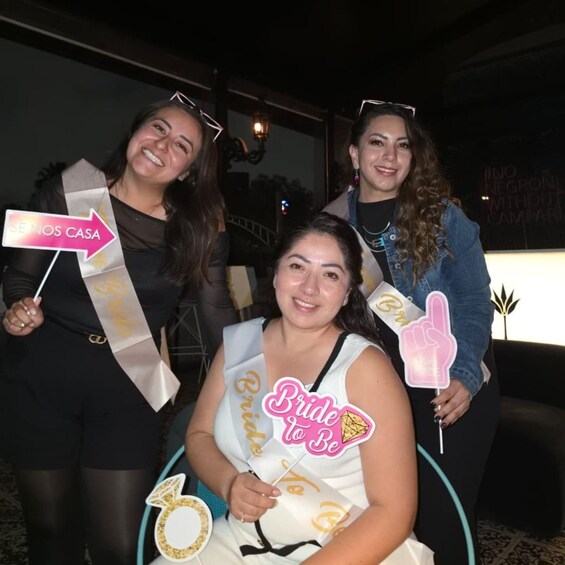 Three people holding signs, one says 'Brides To Be' and another says 'Se Nos Casa'. 2
