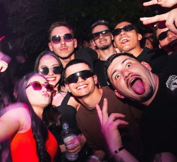 A group of people at an event, some wearing sunglasses and one with a peace sign. 3